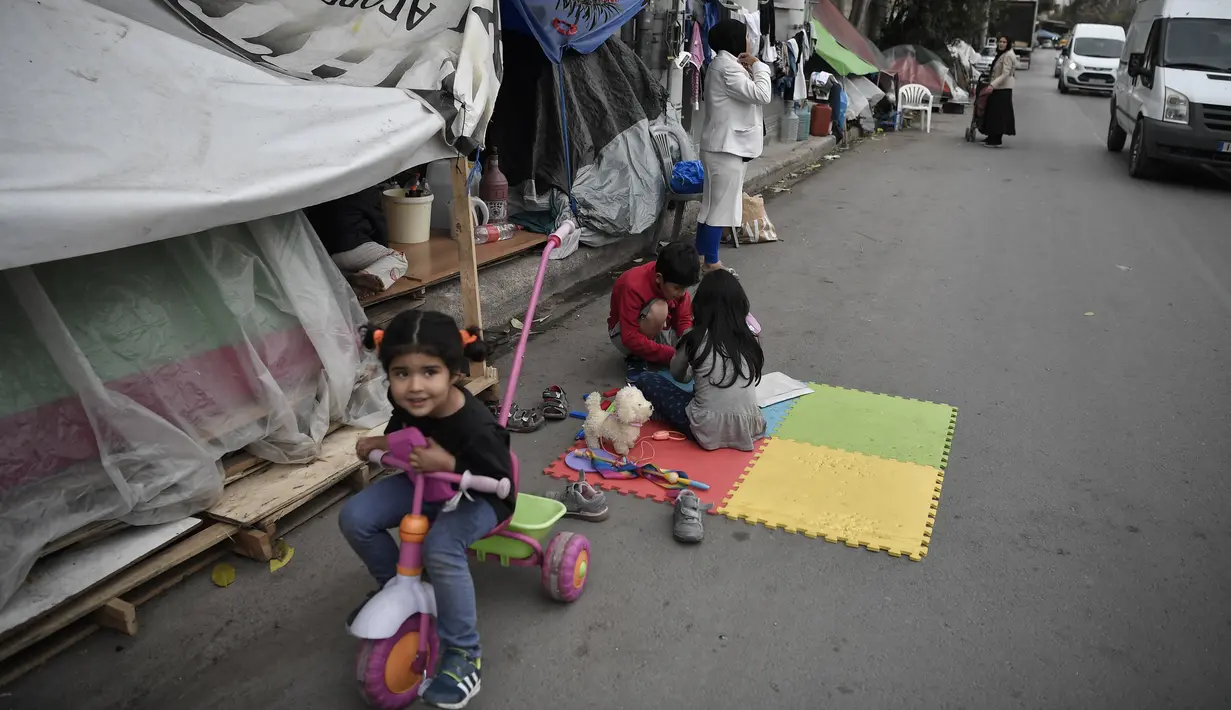 Anak-anak bermain di sebuah jalan di luar kamp pengungsi Eleonas di Athena (20/11/2019). Yunani akan menutup tiga kamp migran terbesarnya di pulau-pulau yang menghadap Turki, dan menggantinya dengan fasilitas baru yang lebih ketat untuk identifikasi, relokasi dan deportasi. (AFP/Louisa Gouliamaki)
