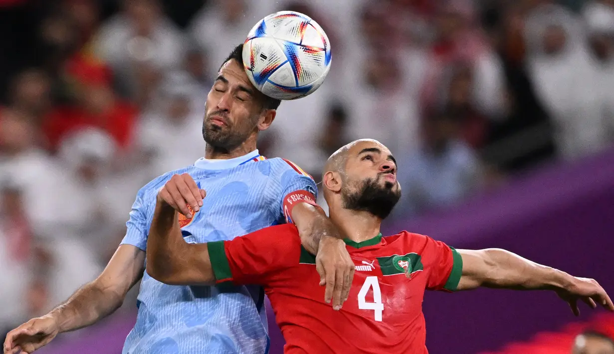 Pemain Maroko, Sofyan Amrabat (kanan) berduel dengan pemain Spanyol, Sergio Busquets pada babak 16 besar Piala Dunia 2022 Qatar di Education City Stadium, Al-Rayyan, 6 Desember 2022. Amrabat menjadi komoditi panas pada bursa transfer musim panas 2023/2024 setelah tampil solid bersama Maroko di Piala Dunia 2022 Qatar. (AFP/Kirill Kudryavtsev)