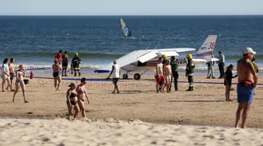 Sejumlah orang berjalan melewati sebuah pesawat kecil yang melakukan pendaratan darurat di pantai Sao Joao yang ramai dekat Lisbon, Portugal, Rabu (2/8). Akibatnya, pesawat itu melindas dua pengunjung pantai yang sedang berjemur. (AP Photo/Armando Franca)