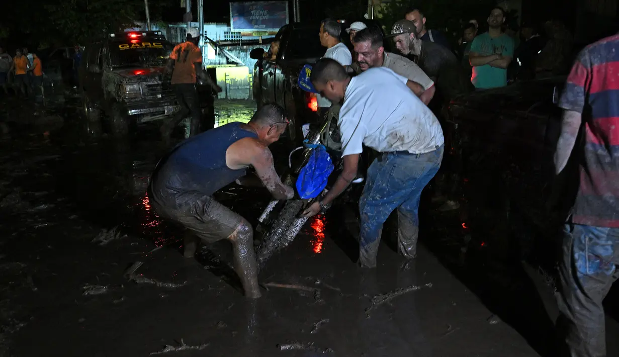 Orang-orang berusaha mengeluarkan sepeda motor yang terjebak di lumpur setelah tanah longsor akibat hujan lebat di El Castaño, Venezuela, Senin (17/10/2022). berbagai pusat pengumpulan sumbangan telah didirikan di ibu kota Venezuela untuk membantu para warga yang telah kehilangan banyak hal akibat bencana tersebut. (Federico Parra / AFP)