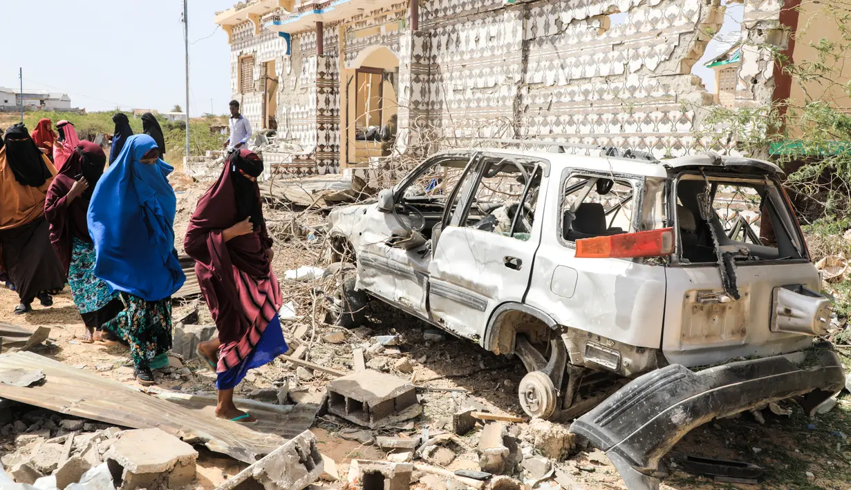 Wanita berjalan di samping rumah yang hancur dan puing-puing mobil menyusul serangan oleh militan Al-Shabaab selama penyerangan ke kantor polisi di pinggiran Mogadishu, Somalia (16/2/2022). (AFP/Hassan Ali Elmi)