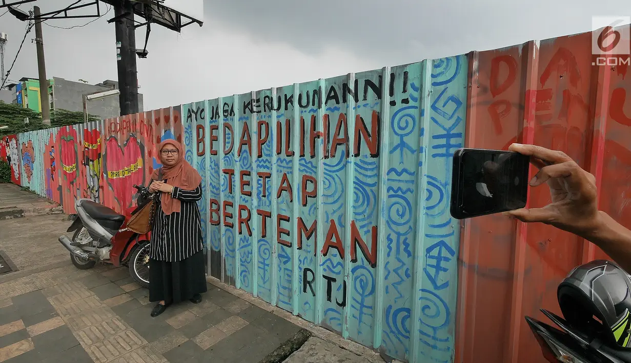 Seorang warga berfoto dengan latar belakang mural di kawasan Margonda, Depok, Sabtu (16/2). Gambar mural memiliki pesan agar masyarakat tetap damai dan berteman meski berbeda dalam memilih calon presiden dalam Pilpres 2019. (Liputan6.com/Herman Zakharia)