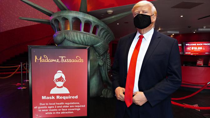 Sosok Donald Trump yang bermasker berdiri di dekat tanda bertuliskan Mask Required' saat Madame Tussauds New York dibuka kembali di New York City, Kamis (27/8/2020). Patung lilin Donald Trump dengan mengenakan masker akan menyambut pengunjung dipintu masuk museum. (Cindy Ord/Getty Images/AFP)