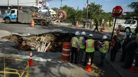 Sejumlah petugas saat menyelidiki sebuah lubang besar (sinkhole) di wilayah Brooklyn, New York, Selasa (4/8/2015). Lubang yang terbentuk di persimpangan pemukiman Sunset Park itu disebabkan erosi dan merusak pipa air serta aspal jalan. (AFP/Kena Betancur)