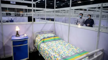 Petugas berdiri di sebelah dinding pemisah antara kamar-kamar yang dipartisi di fasilitas perawatan kesehatan masyarakat di AsiaWorld-Expo di Hong Kong, Selasa (24/11/2020). Rumah sakit darurat khusus corona itu kembali dibuka menyusul lonjakan kasus COVID-19 di Hong Kong. (Anthony WALLACE/AFP)