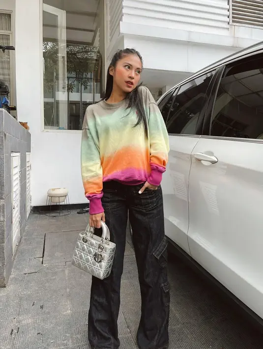 Tyna Kanna tampil berwarna dengan sweater bermotif rainbow yang dipadukan dengan cargo pants warna hitam berdetail jahitan di luar. (Foto: Instagram Tyna Dwijayanti)
