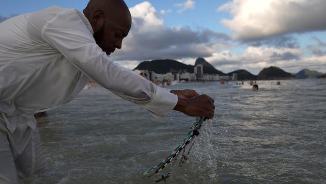 Penganut kepercayaan Afro-Brasil berdoa ketika mencuci kalungnya sebagai simbol perlindungan dalam tradisi upacara penghormatan kepada Dewi Laut, Yemanja di pantai Copacabana, Rio de Janeiro, Sabtu (29/12). (AP/Leo Correa)