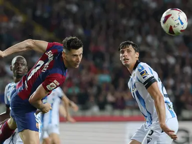 Penyerang Barcelona #09 Robert Lewandowski mengincar bola di samping bek Real Sociedad #24 Robin Le Normand pada laga jornada 35 La Liga 2023/2024 yang dihelat di Estadio Olimpico Lluis Companys, Selasa (14/5/2024) dini hari WIB. (LLUIS GENE / AFP)