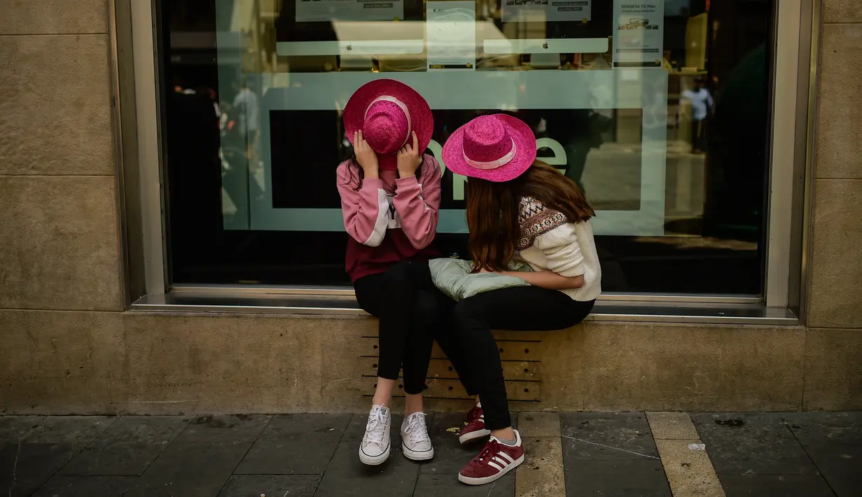 Dua wanita menutupi wajah mereka mengenakan topi saat mencicipi anggur mawar Spanyol untuk mempromosikan minuman tersebut di Pamplona, Spanyol, Sabtu (19/5). (AP Photo/Alvaro Barrientos)