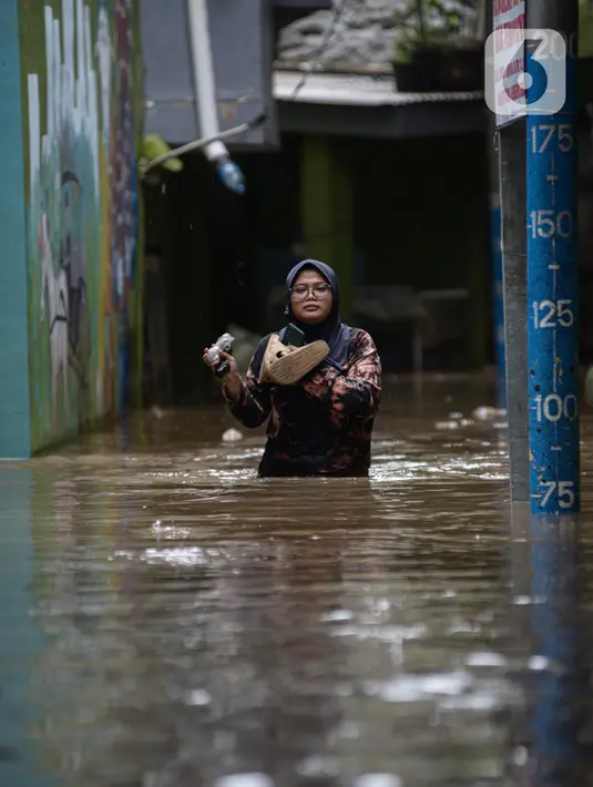 Warga melintasi banjir di kawasan Kebon Pala, Kampung Melayu, Jakarta Timur, Sabtu (16/7/2022). Meskipun ketinggian air sudah mencapai paha orang dewasa, warga setempat belum memutuskan untuk mengungsi. (merdeka.com/Imam Buhori)