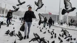 Pejalan kaki melewati kawanan burung di Taksim Square selama badai salju yang menerjang Kota Istanbul, Turki, Sabtu (7/1). Badai salju menyebabkan timbunan salju hingga setinggi 40 centimeter di sebagian wilayah kota itu. (YASIN AKGUL/AFP)