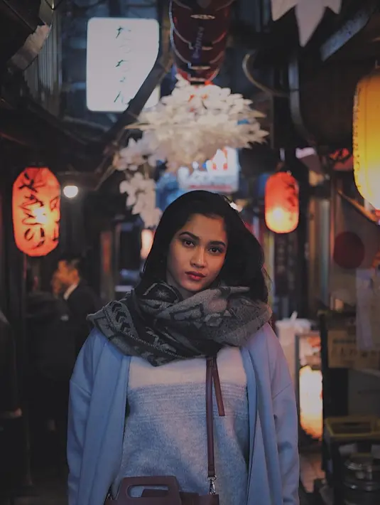 Berpose di jalanan Tokyo dengan latar lampion di depan kedai khas Jepang, wanita kelahiran tahun 1997 ini menggunakan busana berwarna tenang. Kali ini syal berwarna abu-abu bermotif gelap melindungi lehernya dari kedinginan. (Liputan6.com/IG/@aghninyhaque)
