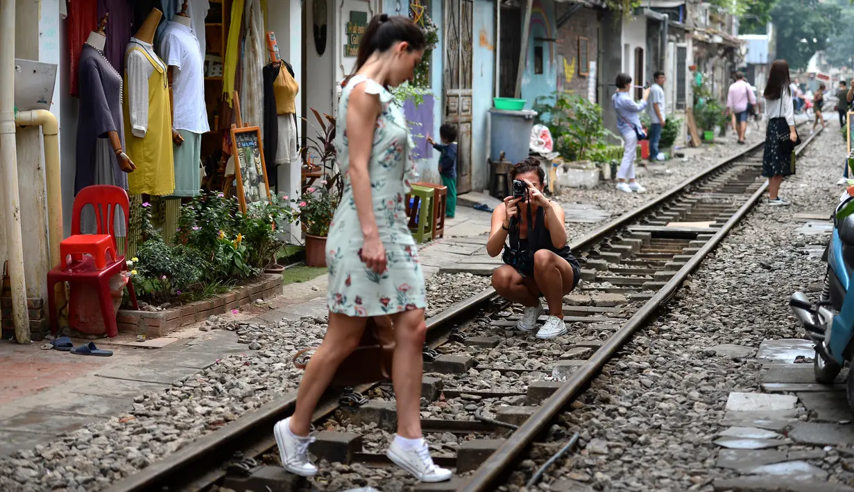 Gambar pada 21 Oktober 2018, turis berfoto di tengah jalur kereta api yang melintasi kawasan permukiman di Hanoi, 20 Oktober 2018. Beberapa tahun terakhir, pengunjung ke kawasan ini lebih menyukai mengambil kesempatan untuk fotografi. (Nhac NGUYEN/AFP)
