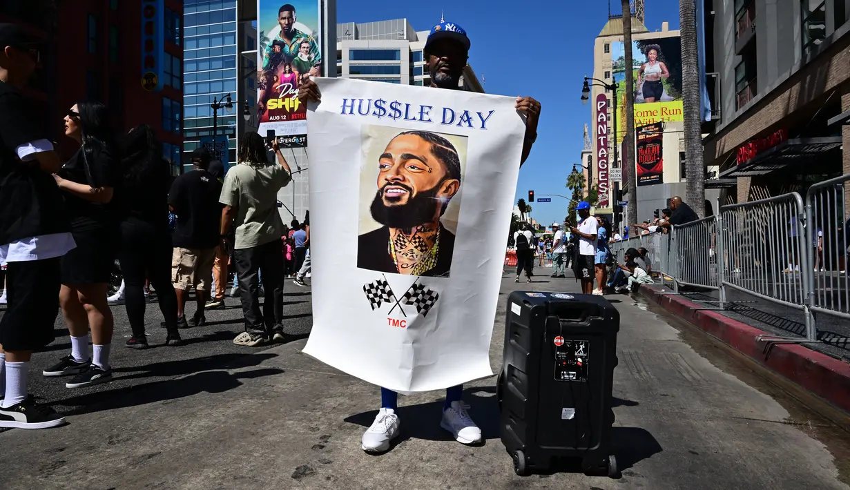 Ronald Nelson menampilkan foto mendiang rapper AS Nipsey Hussle saat orang-orang berkumpul untuk upacara Anumerta Hollywood Walk of Fame Star di Hollywood, California (15/8/2022). Rapper Nipsey Hussle, yang ditembak di Los Angeles tiga tahun lalu , dianugerahi bintang di Hollywood's Walk of Fame pada hari ulang tahunnya yang ke-37. (AFP/Frederic J. Brown)