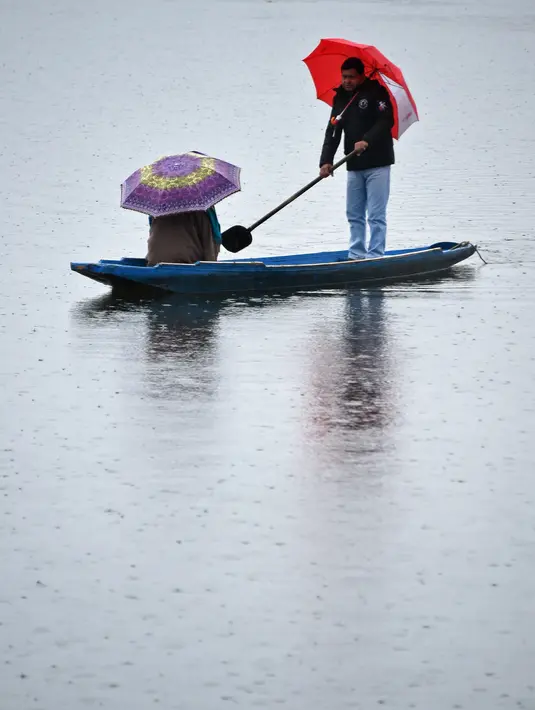 Seorang awak perahu Kashmir mengangkut penumpang saat hujan di Danau Dal di Srinagar (20/3). (AFP Photo/Tauseef Mustafa)
