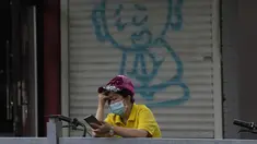 Seorang wanita melihat teleponnya di dekat grafiti yang menggambarkan seorang biarawan di Beijing (24/5/2022). Beijing memperpanjang perintah bagi pekerja dan pelajar untuk tinggal di rumah dan memerintahkan pengujian massal tambahan pada Senin ketika kasus COVID-19 meningkat di ibu kota China. (AP Photo/Ng Han Guan)