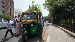 Pejalan kaki berjalan melewati saat pengemudi bajaj Mahender Kumar yang berdiri di kendaraannya dengan 'taman' di atapnya, di New Delhi, India pada 2 Mei 2022. Bajaj kuning dan hijau ada di mana-mana di jalan-jalan New Delhi tetapi kendaraan Mahendra Kumar sangat menonjol -- ia memiliki taman di atapnya bertujuan untuk menjaga penumpang tetap sejuk selama musim panas yang menyengat. (Money SHARMA / AFP)