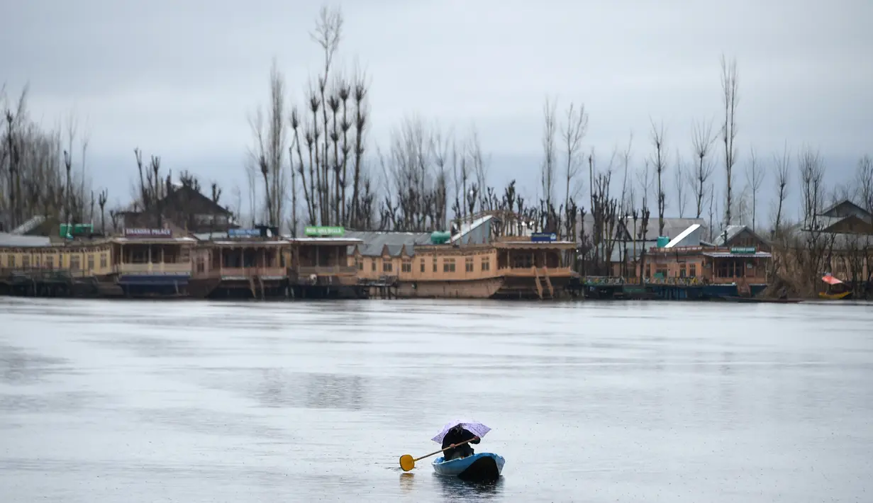 Seorang awak perahu Kashmir memegang payung saat hujan di Danau Dal di Srinagar (20/3). Danau terbesar kedua di propinsi Jammu dan Kashmir ini  merupakan pusat pariwisata dan rekreasi. (AFP Photo/Tauseef Mustafa)