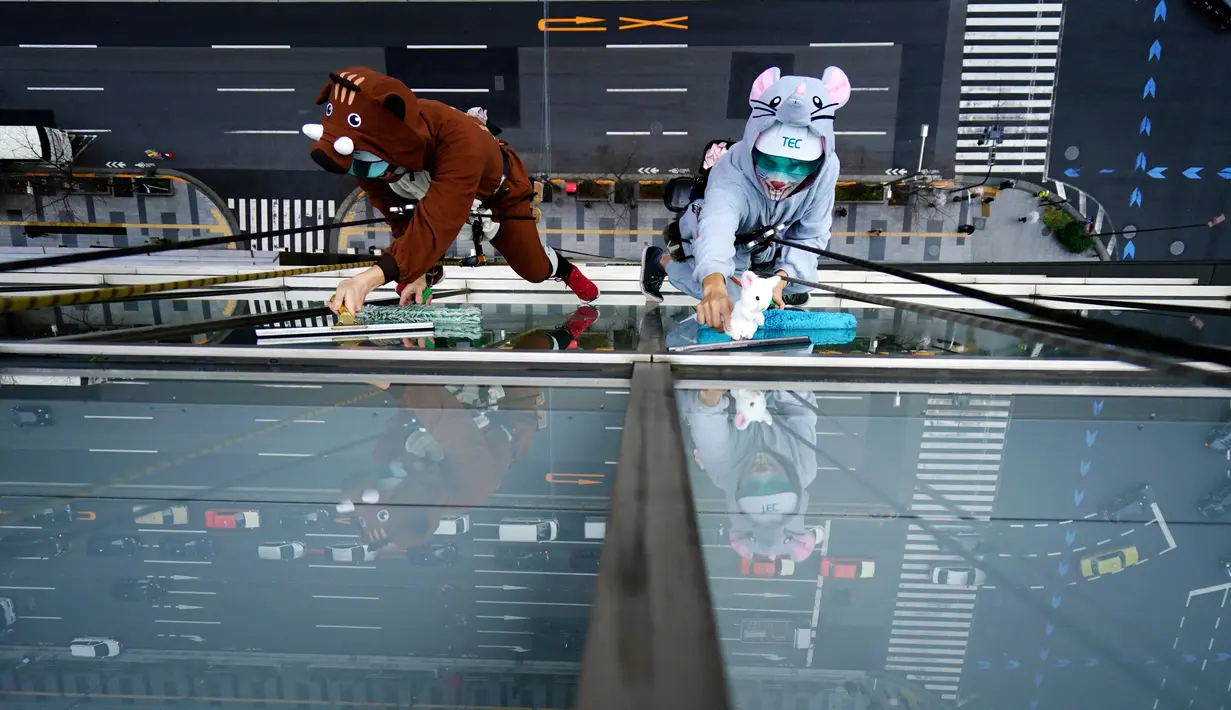 Dua petugas sedang membersihkan kaca jendela  sebuah hotel sambil mengenakan kostum babi hutan dan tikus di Tokyo, Kamis (19/12/2019). Hal ini mereka lakukan untuk merayakan bahun baru Imlek 2019 di Tahun Babi Tanah dan menyambut Tahun Tikus pada 2020. (AP Photo/Eugene Hoshiko)