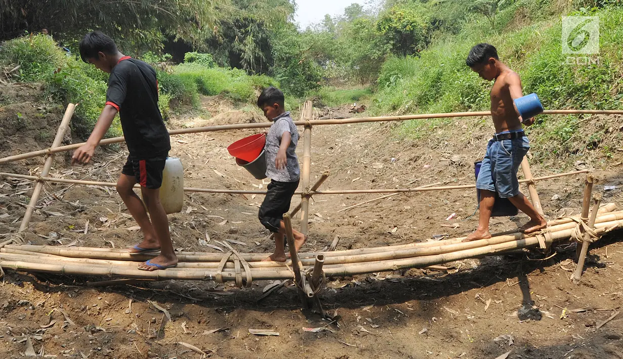 Warga Kampung Gamblok melewati jembatan bambu usai mengambil sisa air Kali Cihoe, Desa Ridomanah, Bekasi, Jawa Barat, Kamis (15/8/2019). Bantuan air bersih dirasa kurang bagi warga sebab distribusi tidak merata dan dilakukan hanya pada awal-awal pemberitaan media massa. (merdeka.com/Arie Basuki)