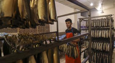 Seorang pemuda Palestina bekerja di fasilitas pengasapan makarel saat ikan itu akan dijual jelang liburan Idul Fitri di Rafah di Jalur Gaza selatan (26/4/2022). Ikan asap makarel menjadi salah satu menu hidangan buka puasa dan Idul Fitri terfavorit bagi warga Gaza selama Ramadhan.(AFP/Said Khatib)