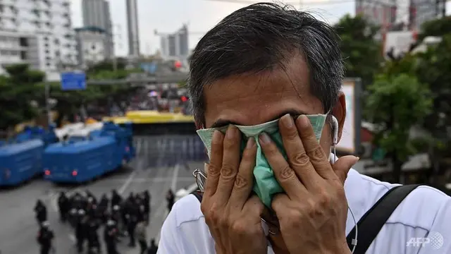 Seorang pria menggunakan masker untuk menyeka wajahnya setelah polisi menggunakan meriam air dengan air berbahan kimia selama rapat umum di dekat parlemen Thailand di Bangkok pada 17 November 2020.