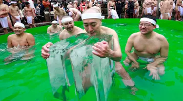 Seorang peserta mandi air dingin memeluk balok es di Teppozu Inari Shinto Shrine di Tokyo, Jepang (8/1). Acara tersebut merupakan ritual musim dingin yang diyakini dapat menjaga kesehatan mereka. (AP Photo/Shizuo Kambayashi)