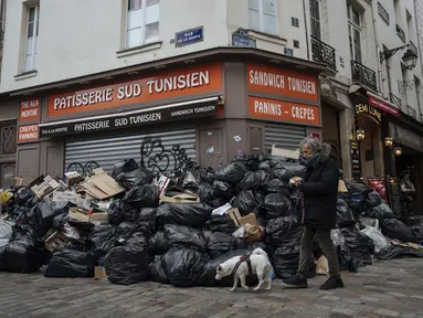 Seorang pria berjalan melewati tumpukan sampah di Paris, Senin (13/3/2023). RUU kontroversial yang akan menaikkan usia pensiun di Prancis dari 62 menjadi 64 tahun mendapat dorongan dengan adopsi tindakan Senat di tengah pemogokan, protes, dan sampah yang tidak diambil menumpuk semakin tinggi dari hari ke hari. (AP Photo/Lewis Joly)