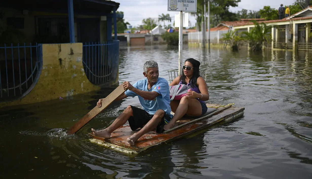 Seorang pria menggunakan pintu sebagai rakit darurat saat dia mengangkut seorang wanita melalui banjir di Mata Redonda, Maracay, Venezuela, Rabu (21/10/2020). Hujan deras di negara bagian Aragua menyebabkan Sungai Madre Vieja meluap dan membanjiri beberapa wilayah. (AP Photo/Matias Delacroix)
