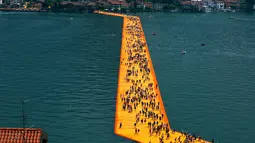 Ribuan wisatawan berjalan di atas instalasi "The Floating Piers" di Danau Iseo, Italia utara, (24/6). Seni instalasi sepanjang 1,9 mil ini terbuat dari 200.000 batu apung yang ditutupi kain oranye. (REUTERS/Stefano Rellandini)
