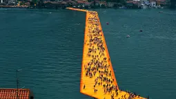 Ribuan wisatawan berjalan di atas instalasi "The Floating Piers" di Danau Iseo, Italia utara, (24/6). Seni instalasi sepanjang 1,9 mil ini terbuat dari 200.000 batu apung yang ditutupi kain oranye. (REUTERS/Stefano Rellandini)