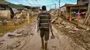 Seorang pria berjalan membawa cangkul di jalanan yang masih berlumpur setelah banjir bandang melanda daerah tersebut di Aceh Tamiang, Provinsi Aceh, pada Sabtu 6 Desember 2025. Gelombang penyakit ancam korban banjir Sumatra di Kabupaten Aceh Tamiang, Provinsi Aceh. (YT HARIONO/AFP)