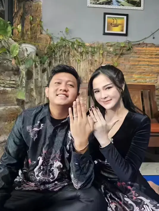 Tampak keduanya tampil serasi mengenakan baju batik nuansa hitam, sembari memamerkan cincin lamaran.