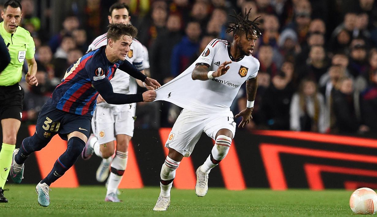 Pemain Barcelona, Gavi (kiri) menarik baju dari pemain MU, Fred saat menggiring bola dalam pertandingan leg pertama play-off babak gugur Liga Europa 2022/2023 yang berlangsung di Camp Nou, Jumat (17/2/2023). (AFP/Josep Lago)