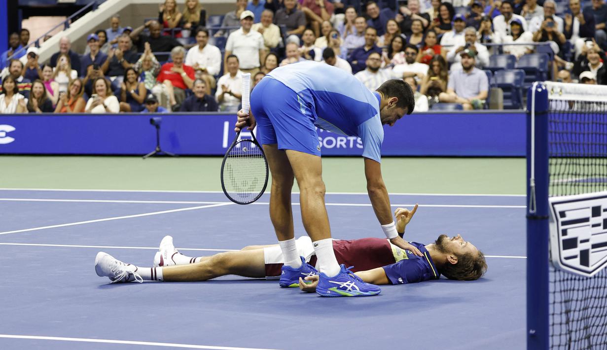 Petenis asal Serbia, Novak Djokovic (atas), menghampiri petenis asal Rusia Daniil Medvedev yang tergeletak di lapangan dalam pertandingan final US Open 2023 yang berlangsung di Arthur Ashe, New York, Senin (11/9/2023) pagi WIB. (AFP/Kena Betancur)