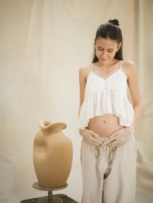 Ia padukan crop top dengan detail ruffle asimetris berwarna putih dan baggy pants cokelat [@angga]