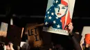 Pengunjuk rasa membawa poster wanita berhijab bendera Amerika saat aksi protes di Bandara Internasional San Francisco, Sabtu (28/1). Mereka memprotes kebijakan Donald Trump yang melarang warga dari 7 negara muslim masuk AS. (AP Photo/Marcio Jose Sanchez)