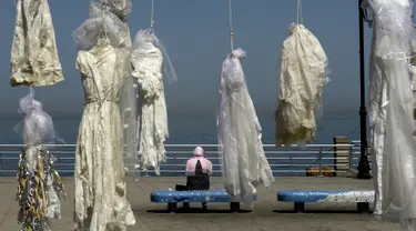 Seorang wanita duduk dekat puluhan gaun pengantin yang digantung di tepi pantai Beirut, Sabtu (22/4). Gaun yang digantung di tepi pantai itu sebagai bentuk protes Undang-Undang Pemerkosaan di Lebanon oleh sekelompok aktivis. (PATRICK BAZ/AFP)