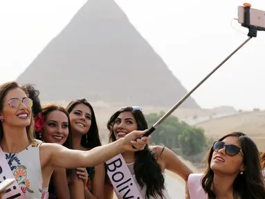 Kontestan Miss ECO Universe berselfie menggunakan tongsis dengan latar belakang segitiga piramida di pinggiran Kairo, Mesir (10/4). Pemenang Miss Eco Universe 2016 akan memenangkan hadiah uang tunai USD 10.000. (REUTERS/Mohamed Abd El Ghany)