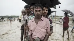 Pengungsi Muslim Rohingya menunggu antrean distribusi makanan saat hujan di kamp pengungsi Nayapara, Bangladesh (6/10). Bangladesh akan membangun kamp pengungsi terbesar di dunia untuk menampung 800.000 orang. (AFP PHOTO/Fred Dufour)