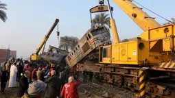 Warga saat melihat proses evakuasi kereta api yang mengalami kecelakaan fatal di Beni Suef, Kairo , (11/2). Badan kereta hingga keluar dari jalur saat alami kecelakaan. (REUTERS / Mohamed Abd El Ghany)