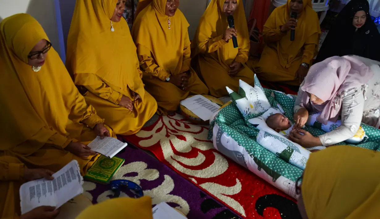 Seorang ibu memegang bayinya saat ritual 'peutron tanoh aneuk' (turun tanah anak) di Banda Aceh, Aceh, Senin (15/7/2019). Ritual turun tanah anak telah menjadi tradisi sakral bagi masyarakat Aceh yang dilaksanakan pada saat bayi berusia 44 hari. (CHAIDEER MAHYUDDIN / AFP)