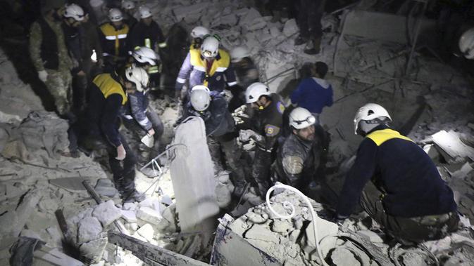 Relawan White Helmets membongkar reruntuhan bangunan mencari korban serangan militer di Provinsi Idlib, Suriah, Minggu, (7/1). Kelompok pemantau dan paramedis mengatakan jumlah korban tewas menjadi 25 orang. (Syrian Civil Defense White Helmets via AP)