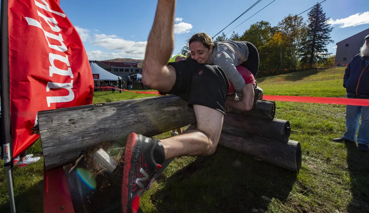 Sebuah tim berjalan melewati rintangan saat mereka berlari selama North American Wife Carrying Championship di Sunday River Resort di Newry, Maine, pada 8 Oktober 2022. Lintasan juga harus memiliki tiga rintangan, yakni dua rintangan kering dan satu rintangan basah berupa kolam lumpur dengan dalam satu meter. (Joseph Prezioso / AFP)