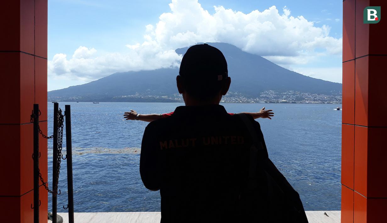 Siluet Direktur Teknis Malut United, Yeyen Tumena, saat mengambil foto salah satu staf klub dengan latar belakang gunung ketika tiba di pelabuhan Tidore, Maluku Utara. (Bola.com/Okie Prabhowo)