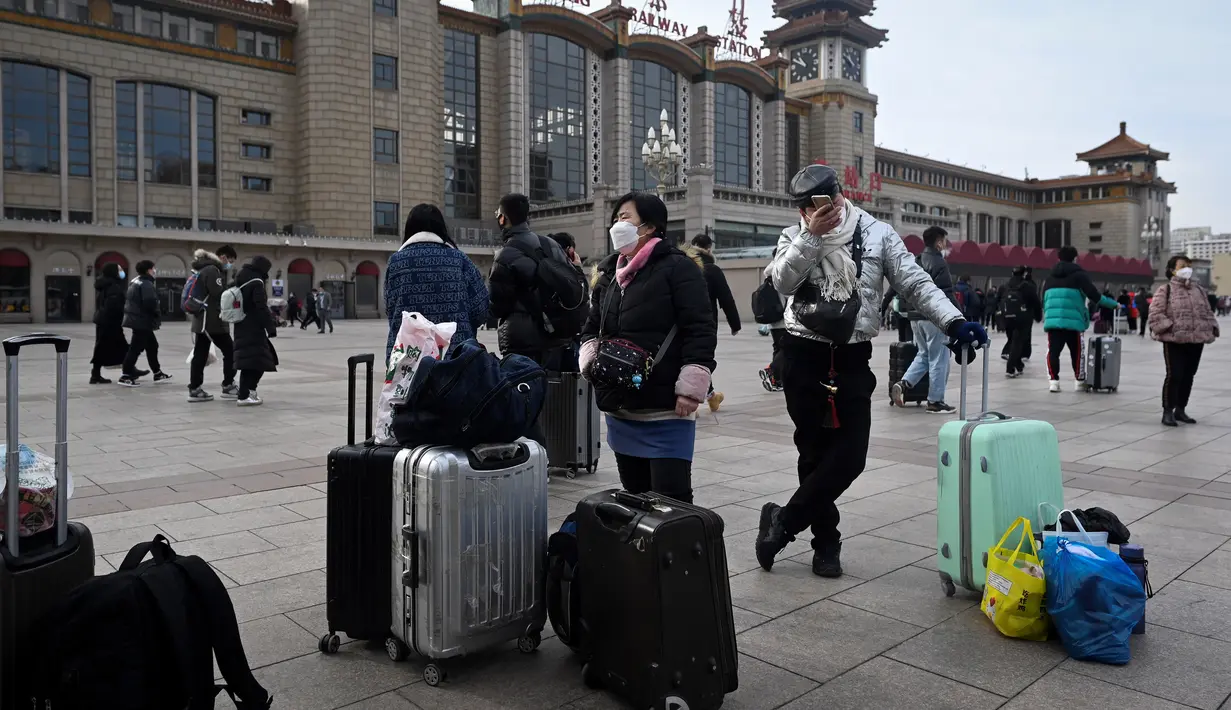 Penumpang membawa tas menunggu kereta di luar pintu masuk stasiun kereta api Beijing di ibu kota China (7/1/2023). Ketika migrasi tahunan dimulai dengan orang-orang yang kembali ke kampung halaman mereka untuk perayaan Tahun Baru Imlek. (AFP/Wang Zhao)