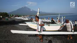 Nelayan mengangkat perahu dengan latar Gunung Agung yang mengeluarkan asap tebal dari kawasan Amed, Karangasem, Bali, Kamis (7/12). Sepekan terakhir, aktivitas Gunung Agung mulai tampak tenang, meskipun masih status Awas. (Liputan6.com/Immanuel Antonius)
