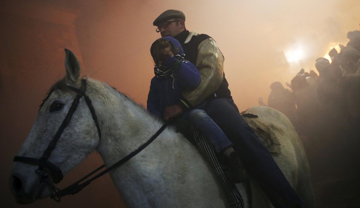 Seorang pria membawa anaknya dalam perayaan " Luminarias " di desa San Bartolome de Pinare, Spanyol, (16/1).  Tradisi sudah ada 500 tahun lalu di desa ini. (REUTERS / Susana Vera)