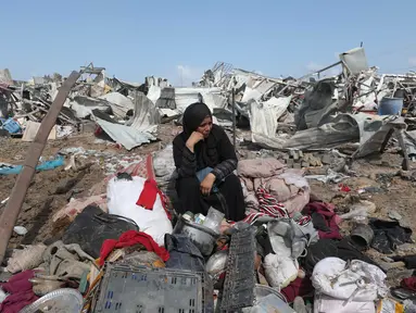 Seorang wanita Palestina yang terpaksa mengungsi duduk bersama barang-barangnya setelah serangan Israel di kamp pengungsi Deir el-Balah, Jalur Gaza tengah, pada 21 Agustus 2025. (Eyad BABA/AFP)