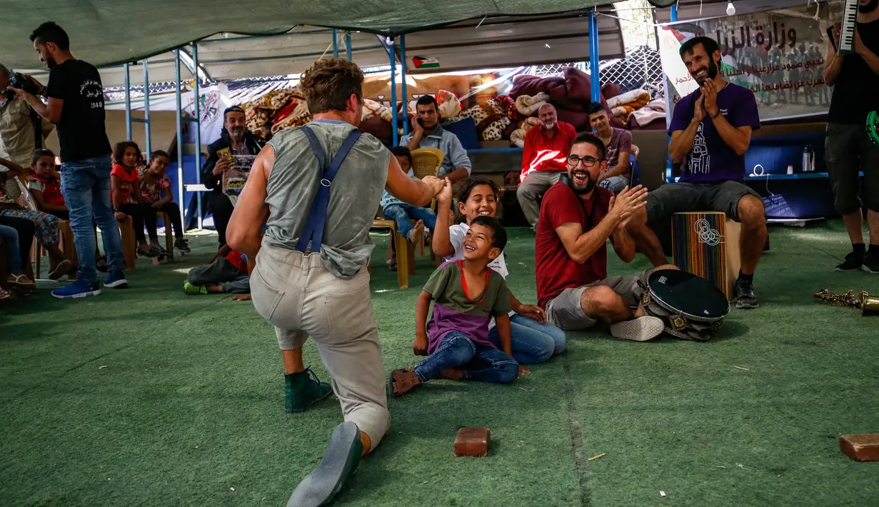 Anak-anak Palestina bermain dengan rombongan badut Spanyol yang tampil menghibur di desa suku Bedouin, Tepi Barat, 22 September 2018. Atraksi ini dilakukan lantaran desa di dekat permukiman Israel itu akan digusur Israel pada Oktober. (AFP/ABBAS MOMANI)